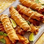Taquitos on a platter with plates in the background.