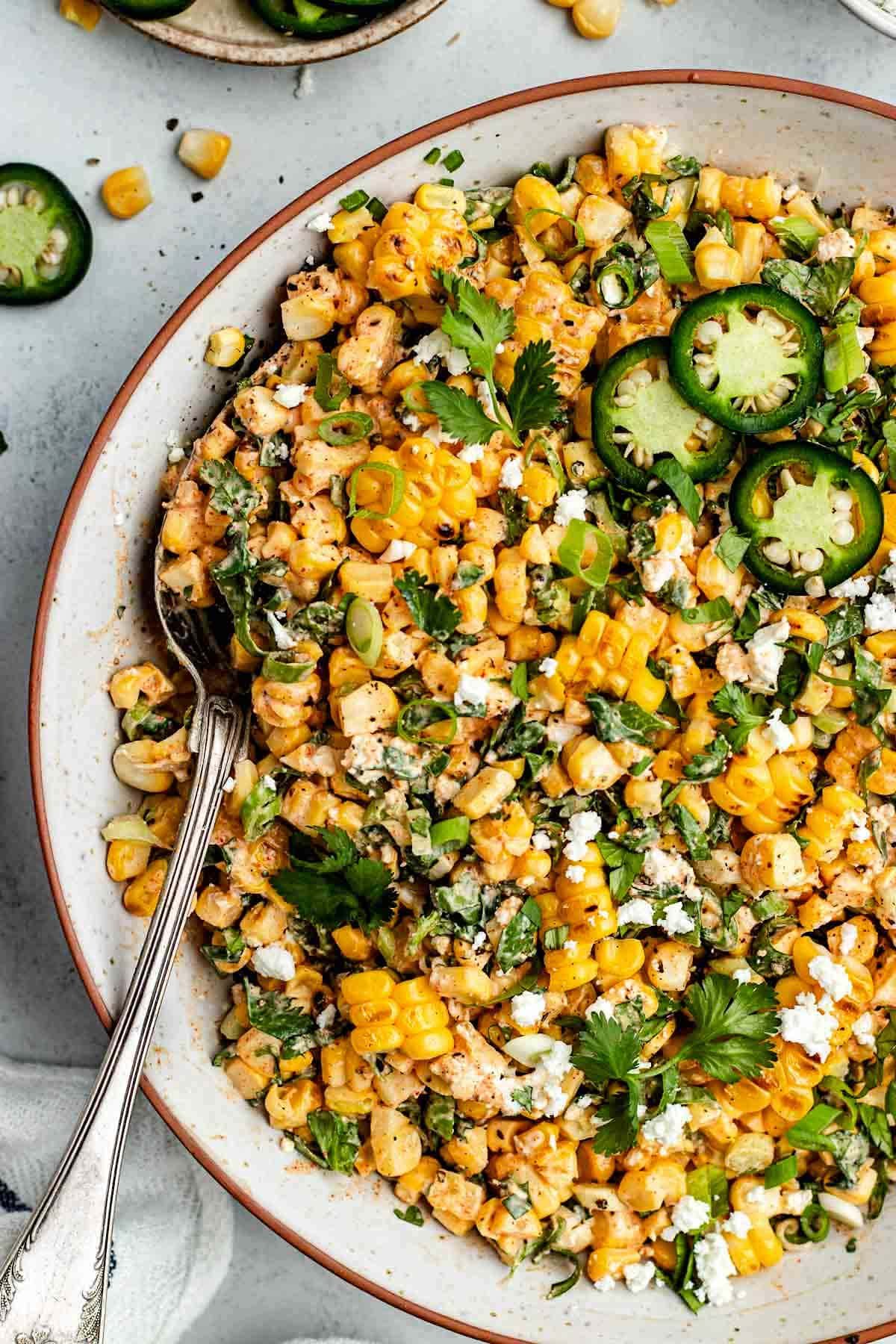 close up of Mexican corn salad in bowl with serving spoon.