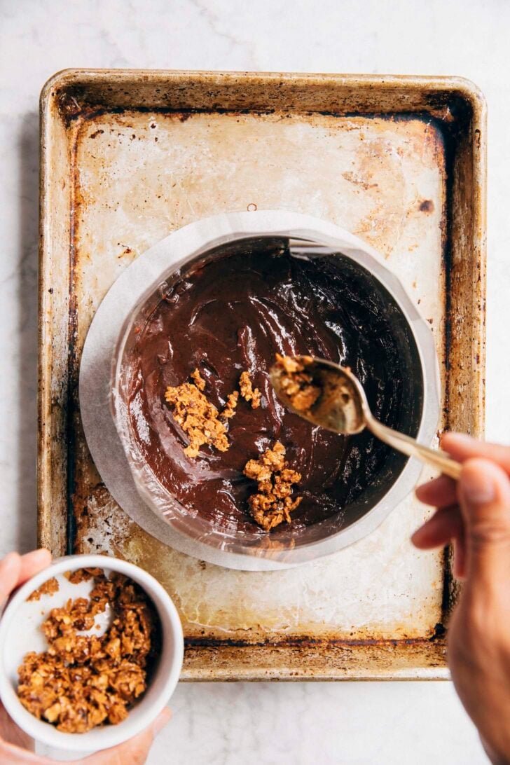 photo showing the chocolate ganache layer being topped with hazelnut crunch