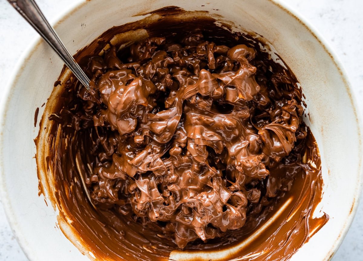 pretzels and dates being coated in melted chocolate and peanut butter in bowl.