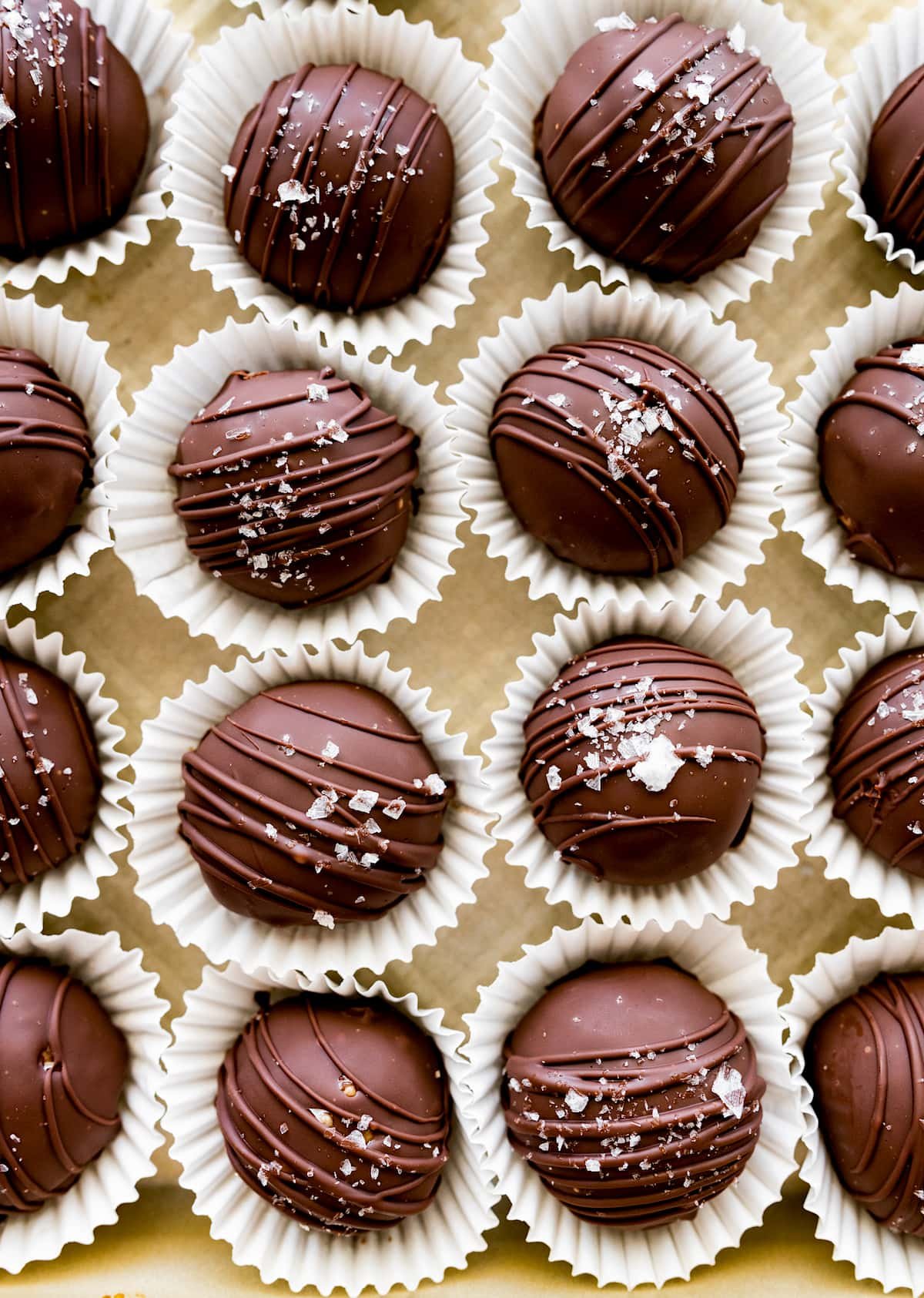 peanut butter protein balls covered in chocolate and sprinkled with flaky sea salt in mini paper cups.