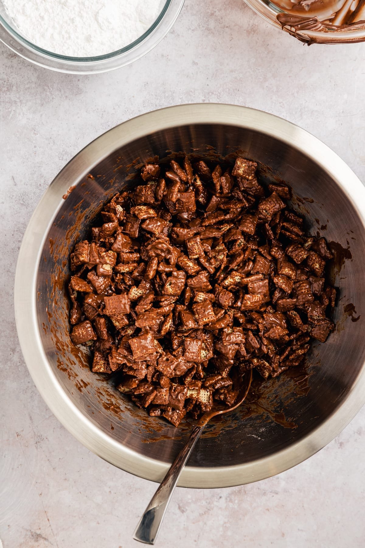 Homemade Puppy Chow is easy to make and SO addicting. This recipe for chocolate peanut butter-covered Chex cereal is a perfect party snack! Chex cereal coated in a chocolate peanut butter mixture in a large metal bowl.