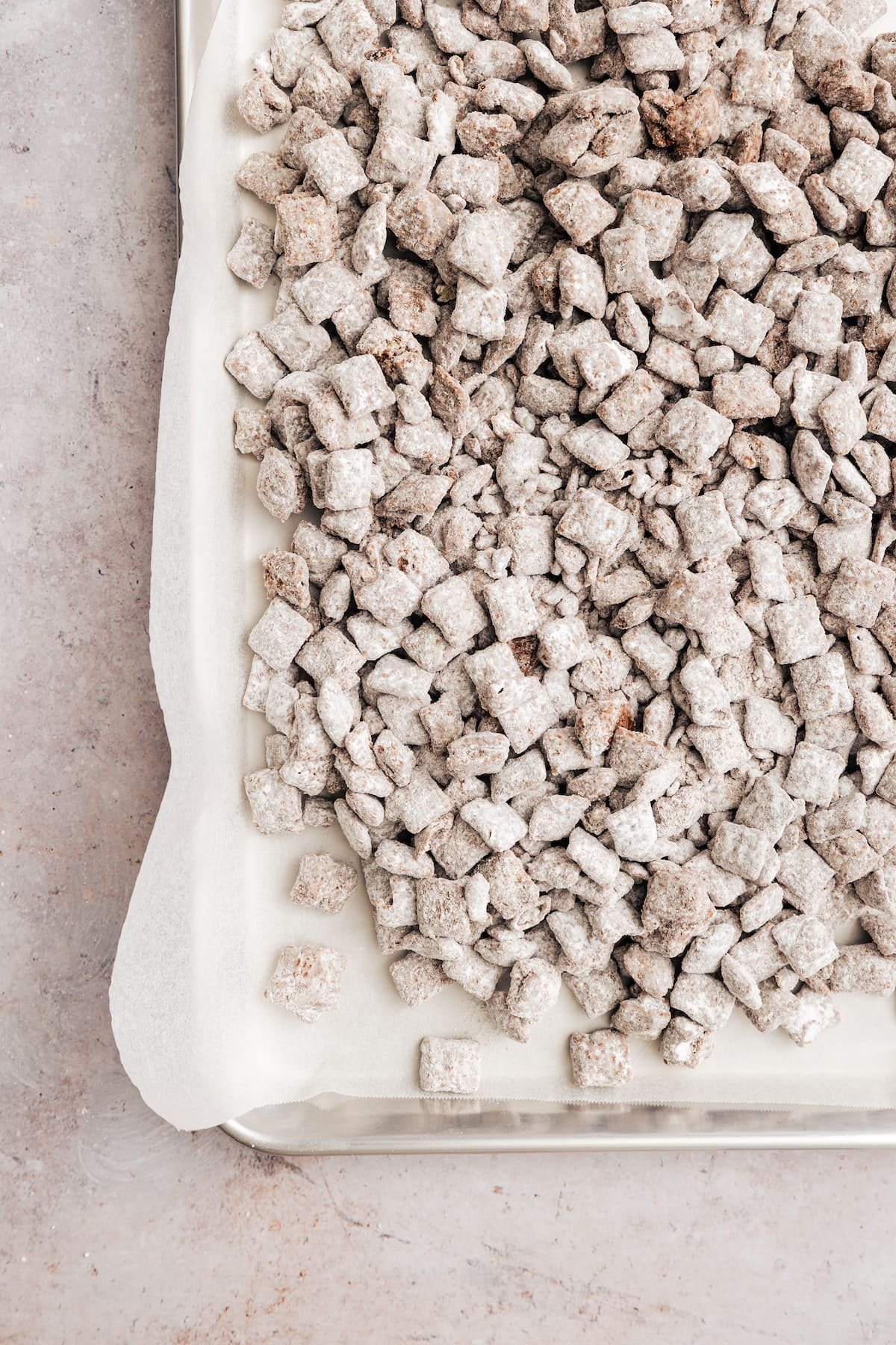 Homemade Puppy Chow is easy to make and SO addicting. This recipe for chocolate peanut butter-covered Chex cereal is a perfect party snack! Overhead view of puppy chow on a parchment-lined baking sheet.