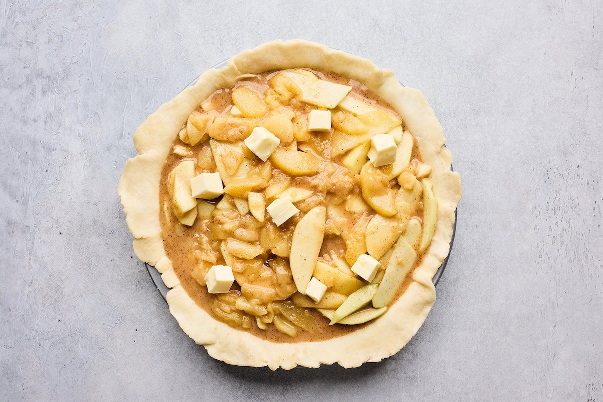 assembling apple pie with butter cubes on top.