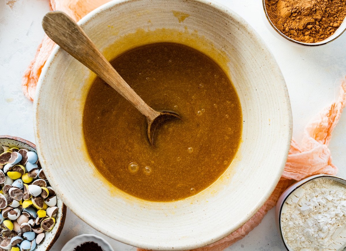 liquid ingredients in mixing bowl with wooden spoon to make cadbury egg brownies. 