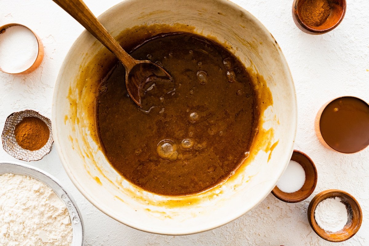 brown butter, brown sugar, eggs, and vanilla being mixed together in bowl with wooden spoon. 