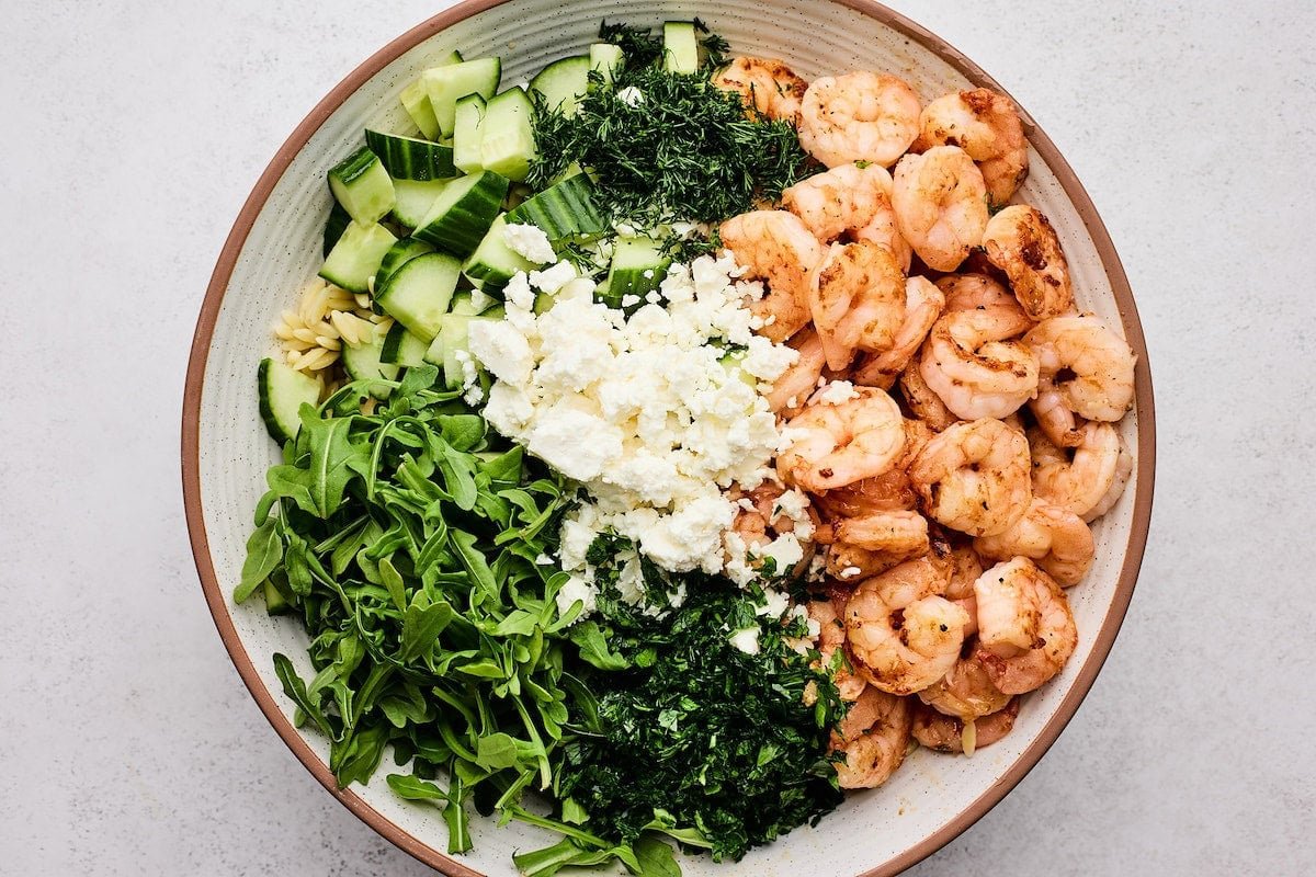 shrimp, arugula, herbs, feta cheese, cucumber, and orzo in serving bowl. 