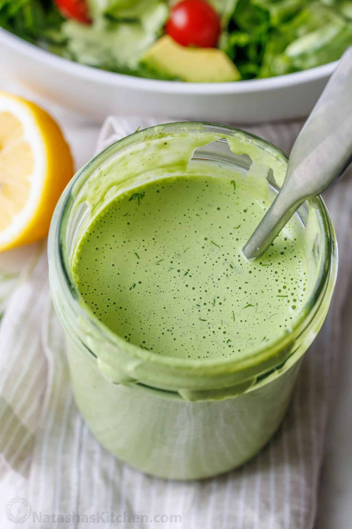 Green Goddess Salad Dressing in a mason jar mixed with a spoon and dotted with tiny specs of dill.