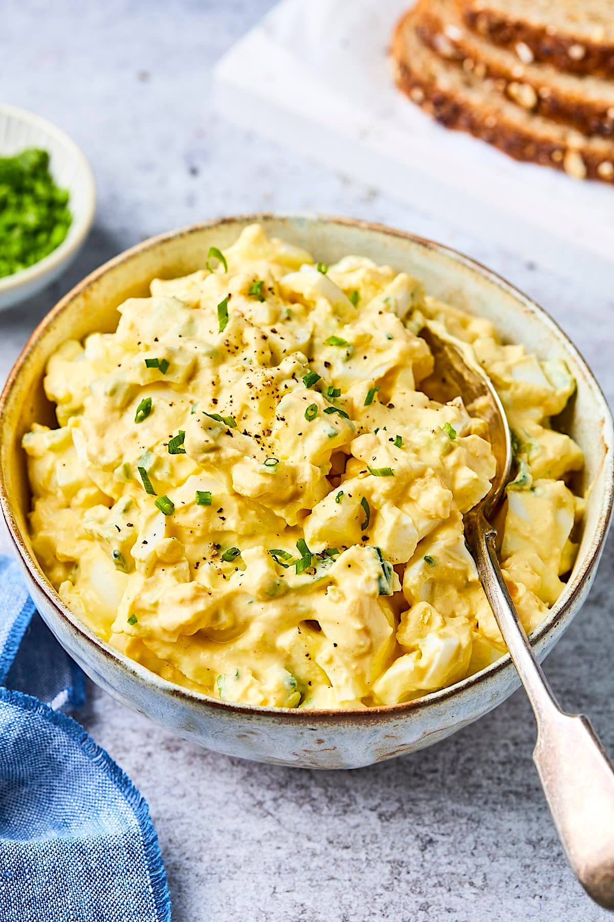 egg salad in bowl with chives and a spoon. 