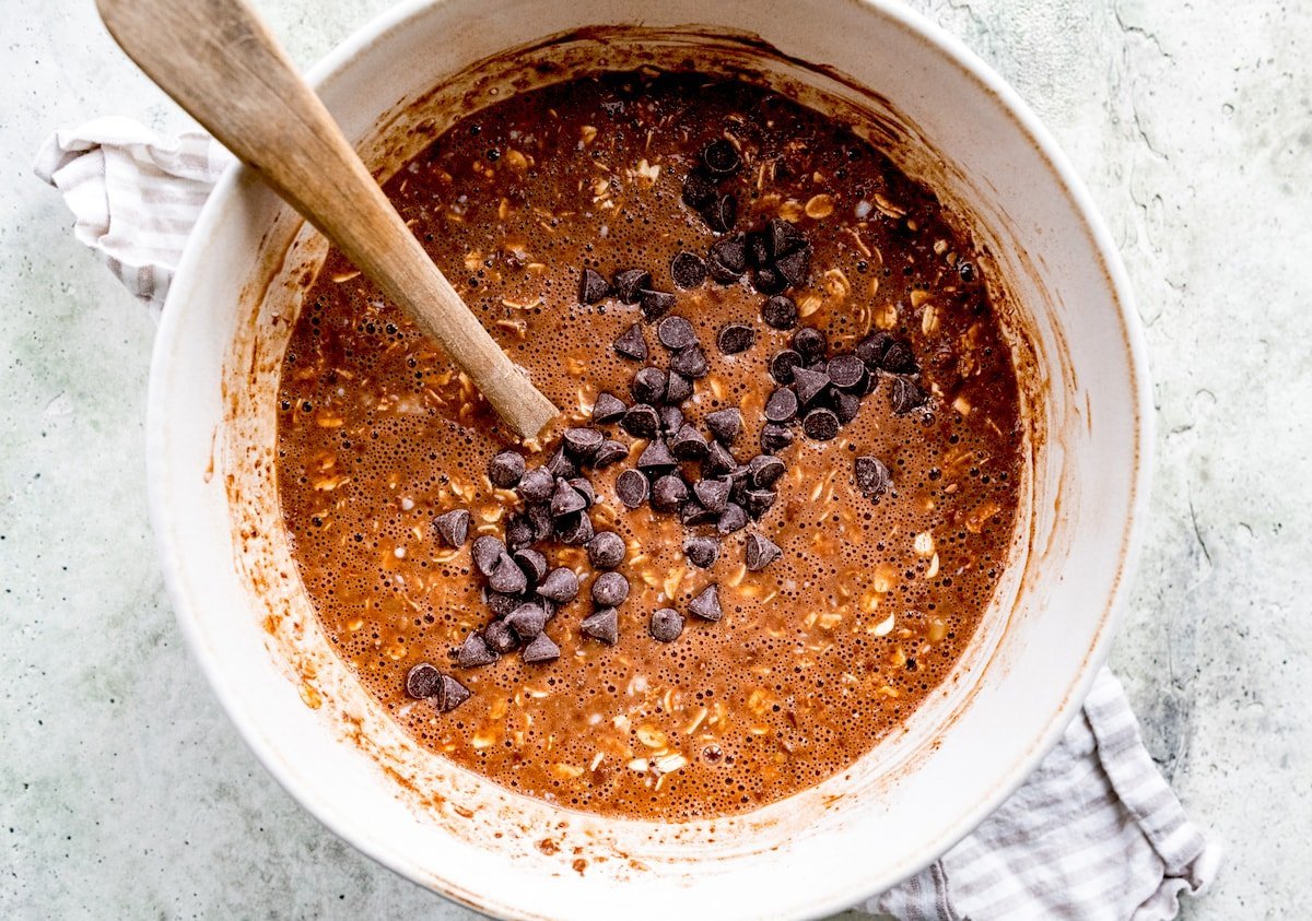 chocolate banana baked oatmeal ingredients in mixing bowl with chocolate chips and wooden spoon.
