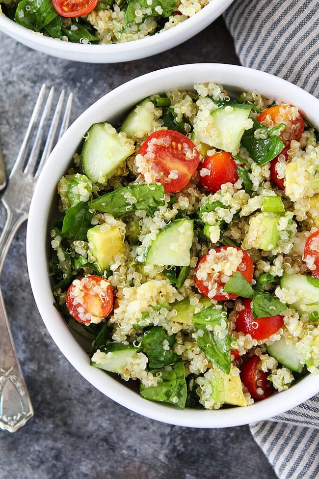 Easy Quinoa Salad is the BEST quinoa salad recipe! It is great for lunch, dinner, or the perfect side dish for potlucks and parties. #quionasalad #quinoa #salad #vegan #vegetarian #glutenfree #healthyrecipe #easyrecipe #veganrecipes #saladrecipe #salad close up of quinoa salad in bowl with spinach, cucumber, tomatoes, avocado, and green onion.
