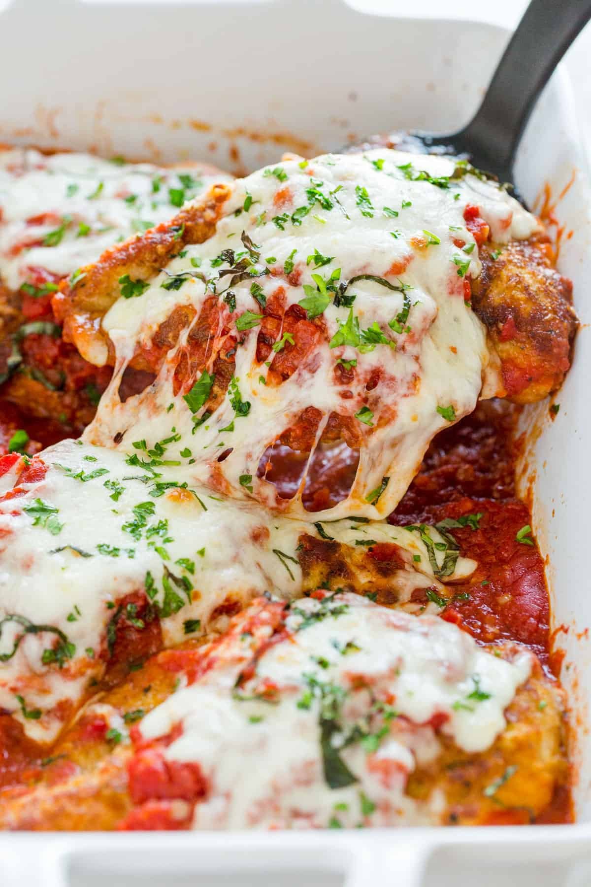 How to make the best Chicken Parmesan with tender juicy chicken topped with marinara and cheese - just like your favorite Italian restaurant. Chicken Parmigiana being served out of a casserole dish with spatula and cheese pull