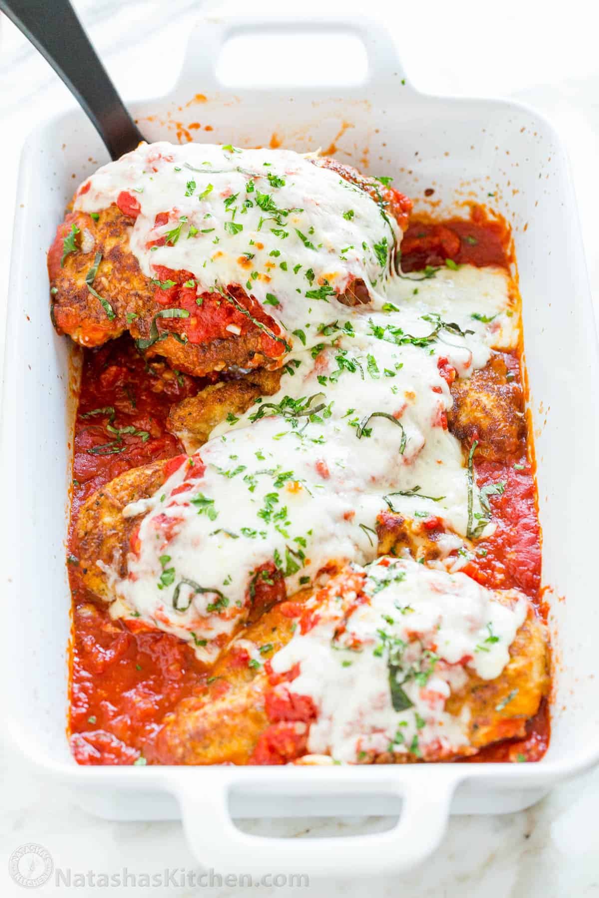 How to make the best Chicken Parmesan with juicy chicken, crisp crust, topped with marinara and melty cheese - a classic restaurant remake! Chicken parmesan served out of white casserole dish with spatula