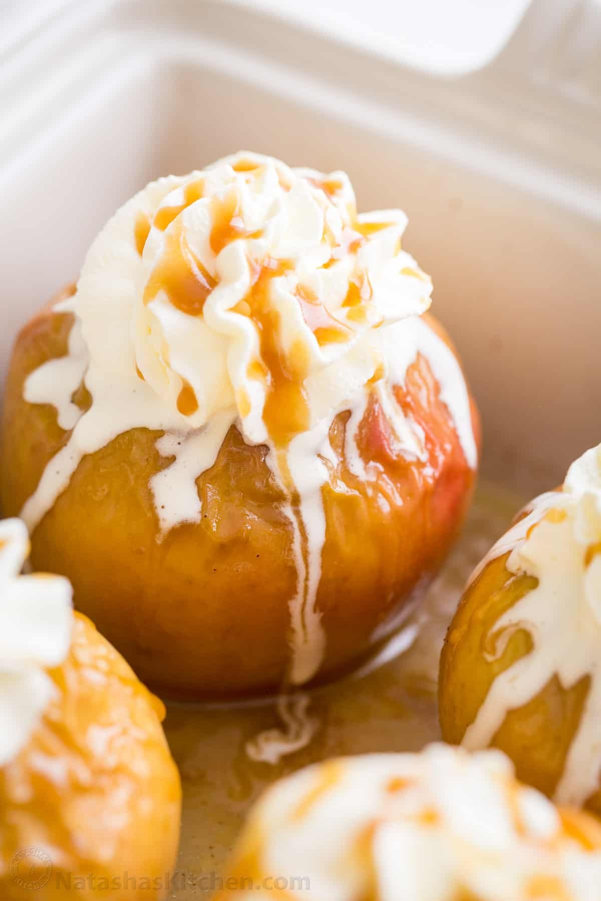 These cozy Baked Apples are infused with fall flavor inside and out. Stuffed with cinnamon sugar, they taste just like apple pie filling! Baked apples in a baking dish topped with whipped cream and caramel sauce.
