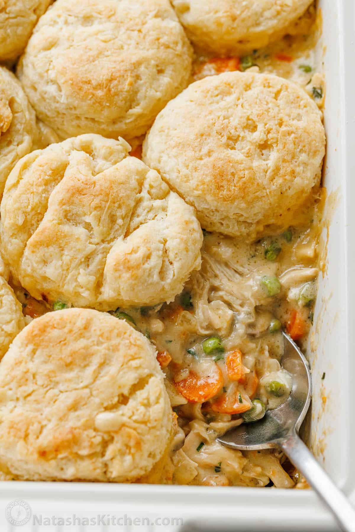 Chicken Pot Pie Casserole has all the cozy flavor of chicken pot pie, but it's even easier topped with flaky biscuits. Overhead close up view of a spoon scooping a serving of chicken pot pie casserole from a baking dish.