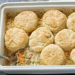 Baked chicken pot pie casserole in a baking dish topped with biscuits, with a serving missing.