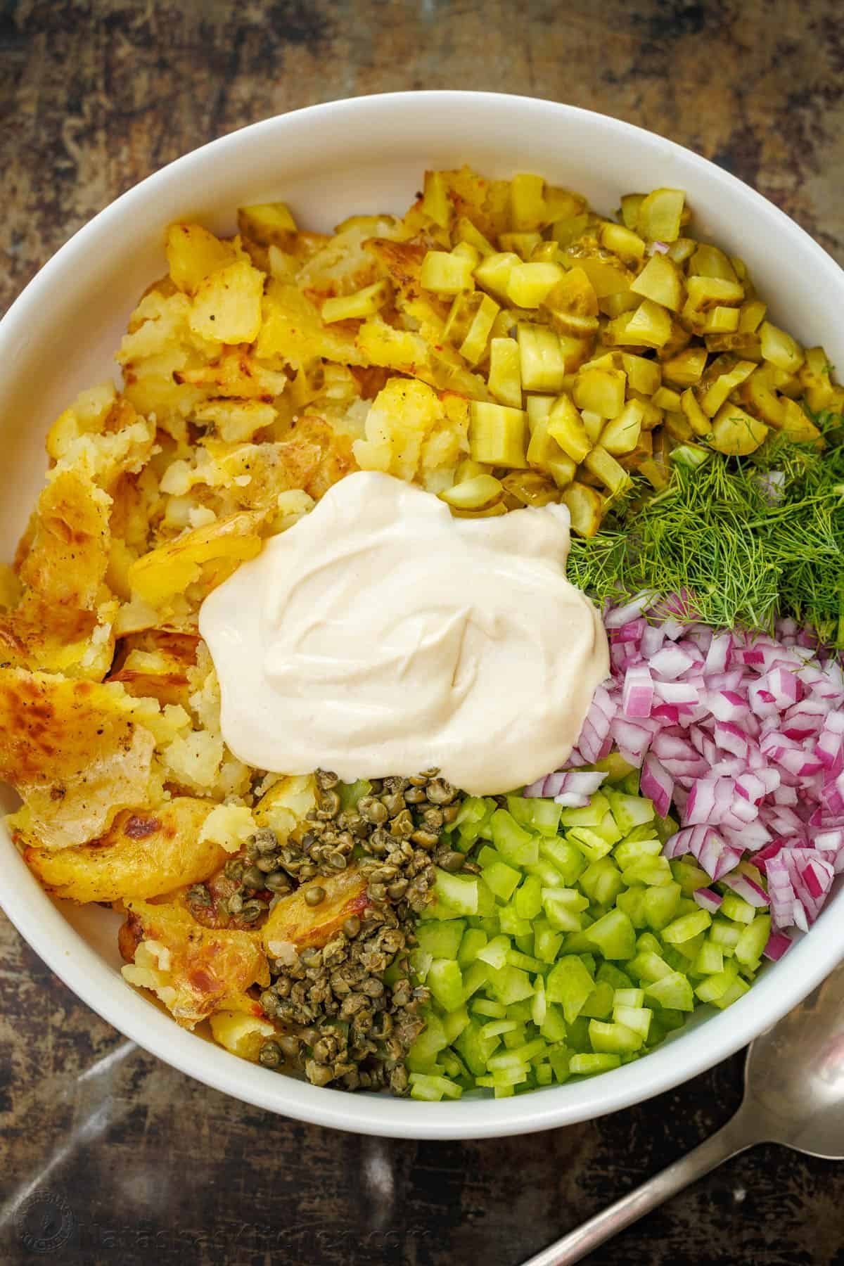 Smashed Potato Salad: A crispy twist on potato salad, with crisp vegetables and fresh herbs, combined with an irresistible two-ingredient dressing. This light and satisfying dish will win you over with every bite. Smashed Potato Salad ingredients in a bowl, ready to mix with the two ingredient mayonnaise based dressing