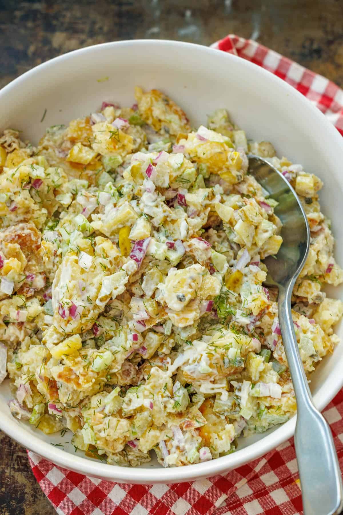 Smashed Potato Salad: A crispy twist on potato salad, with crisp vegetables and fresh herbs, combined with an irresistible two-ingredient dressing. This light and satisfying dish will win you over with every bite. Smashed Potato Salad in a bowl with a serving spoon, garnished with fresh dill.