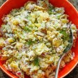 Smashed Potato Salad in a red serving bowl with a serving spoon, garnished with fresh dill.