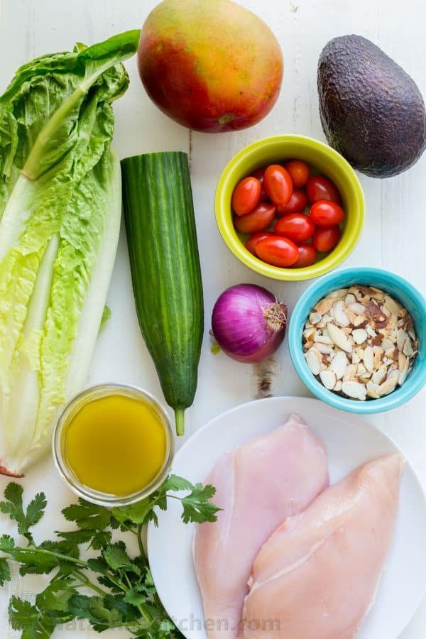 Ingredients for chicken mango avocado salad with mango, avocado, cucumber, tomato, almonds, romaine, chicken breast and honey vinaigrette ingredients to make mango salad.