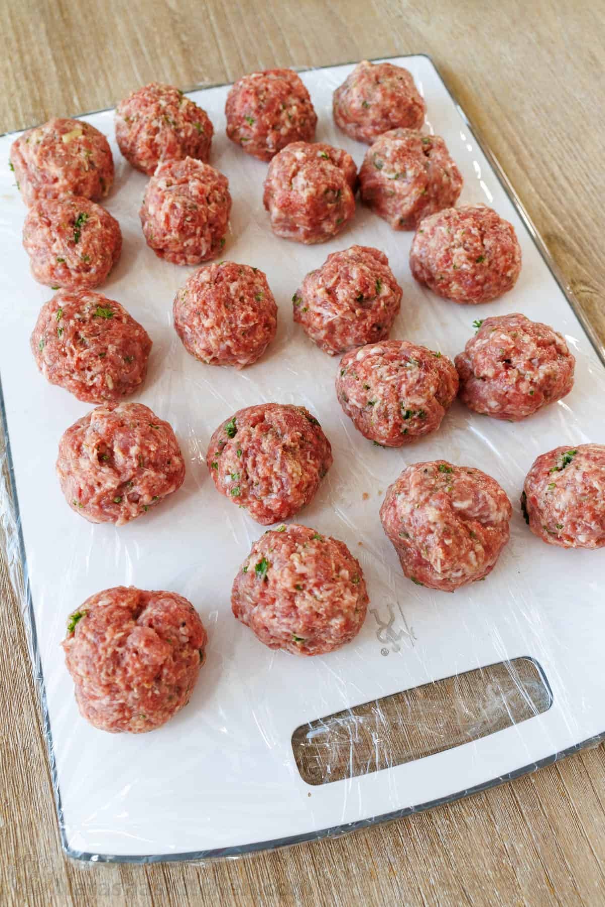 This Meatballs Parmesan Recipe combines the best Italian dishes into one, delicious and easy dish. Homemade Meatballs ready in just an hour! Raw Meatballs rolled into golf-ball size balls and lined up on a white cutting board to be cooked.