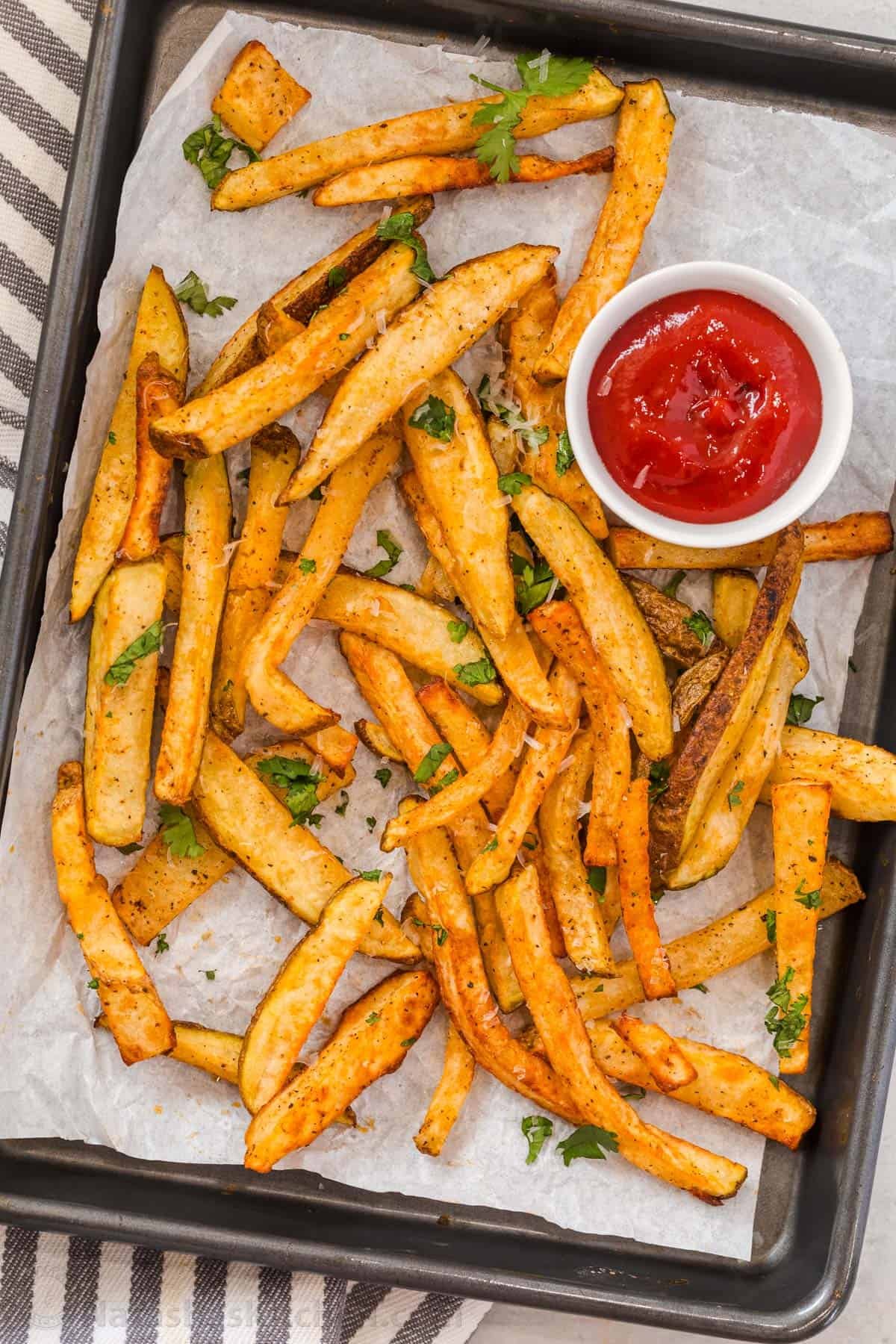 Homemade Air Fryer French Fries are so easy to make and taste much better than frozen fries! The Air Fryer makes it quick and easy to serve. Sliced potatoes on parchment with ketchup