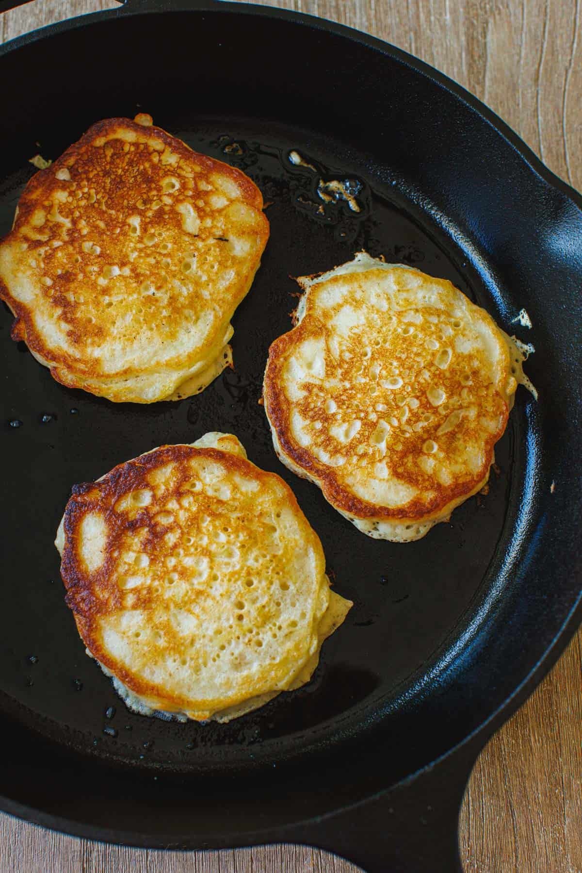 Browned apple pancakes cooking in a cast iron skillet.