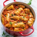 Stuffed cabbage rolls inside a red Dutch oven, covered in Podliva sauce.