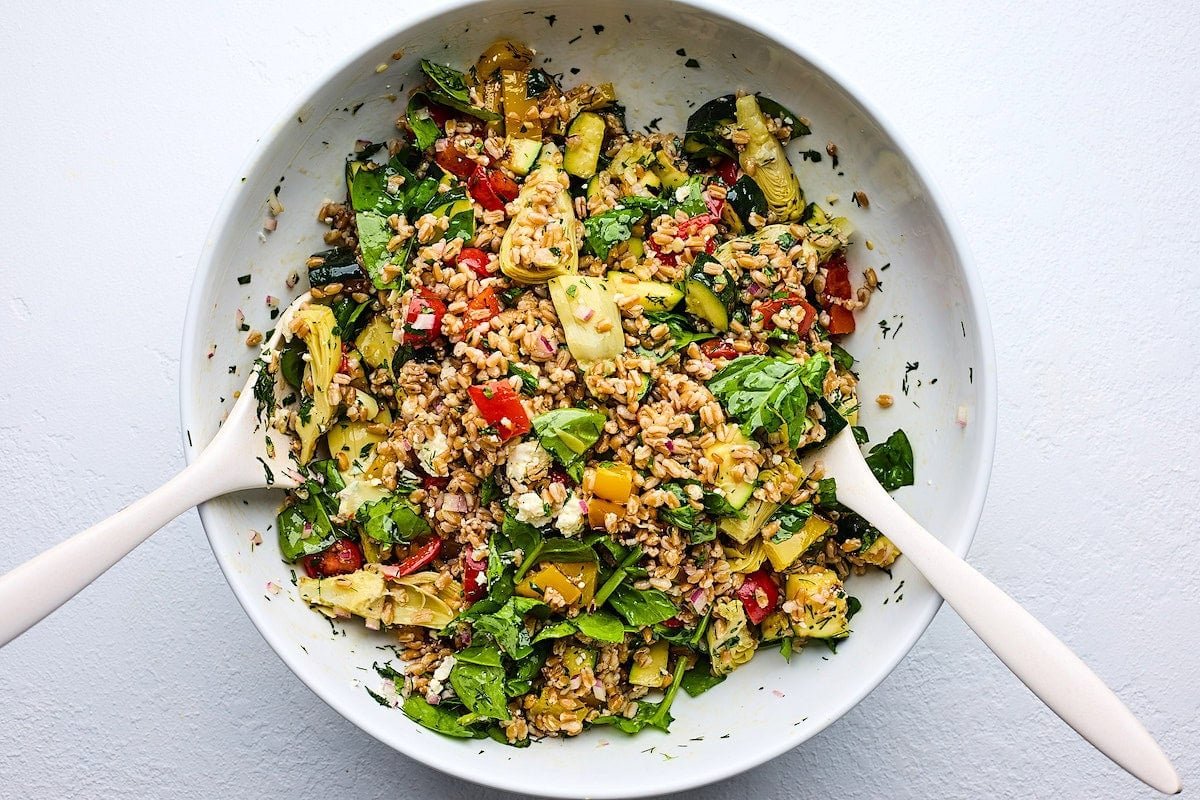 grilled vegetable farro salad in serving bowl with salad servers. 