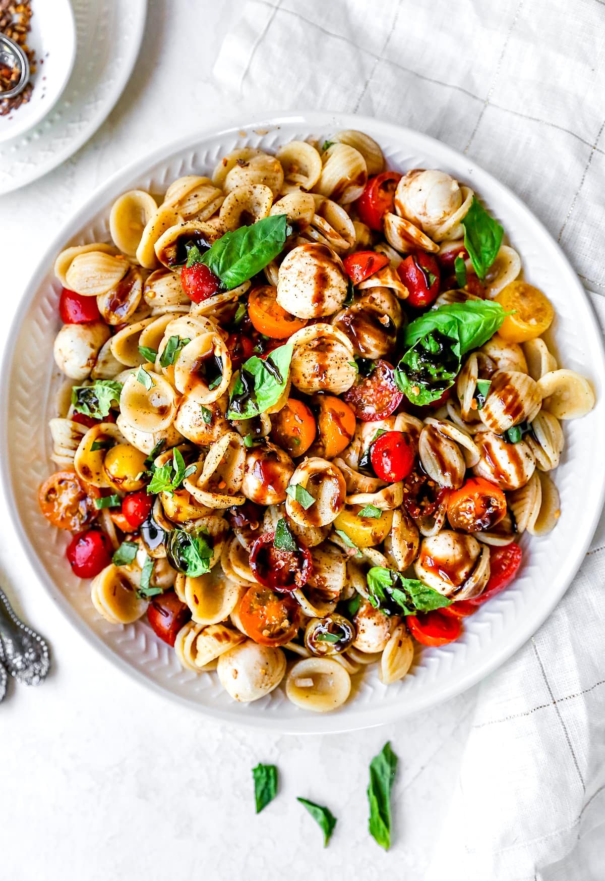 caprese pasta salad in bowl with balsamic glaze, tomatoes, fresh mozzarella, and basil. 