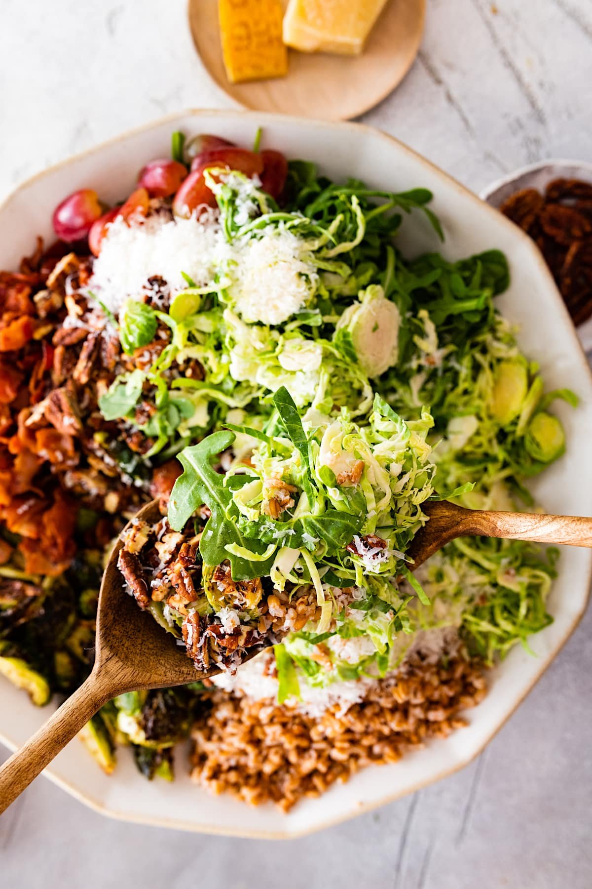 shredded brussels sprout salad with bacon in bowl with wood salad servers. 