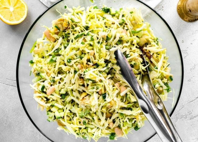 crispy artichoke white bean salad in bowl with tongs
