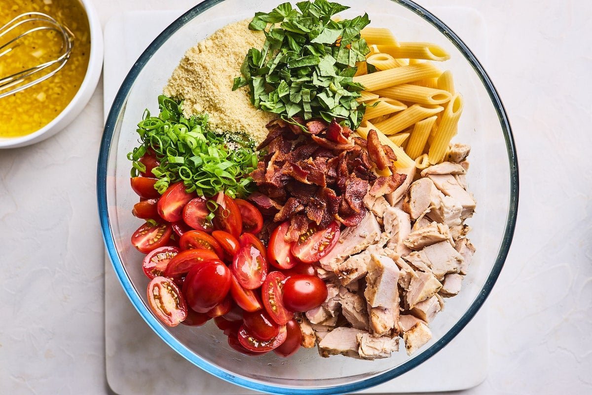 chicken pasta salad ingredients in mixing bowl with dressing on the side in bowl.