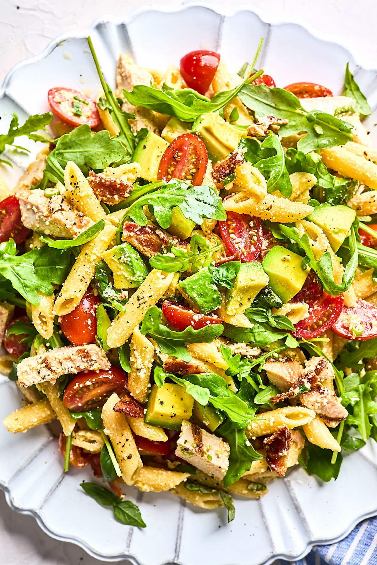 chicken pasta salad with arugula, tomatoes, avocado, and Parmesan cheese on plate.