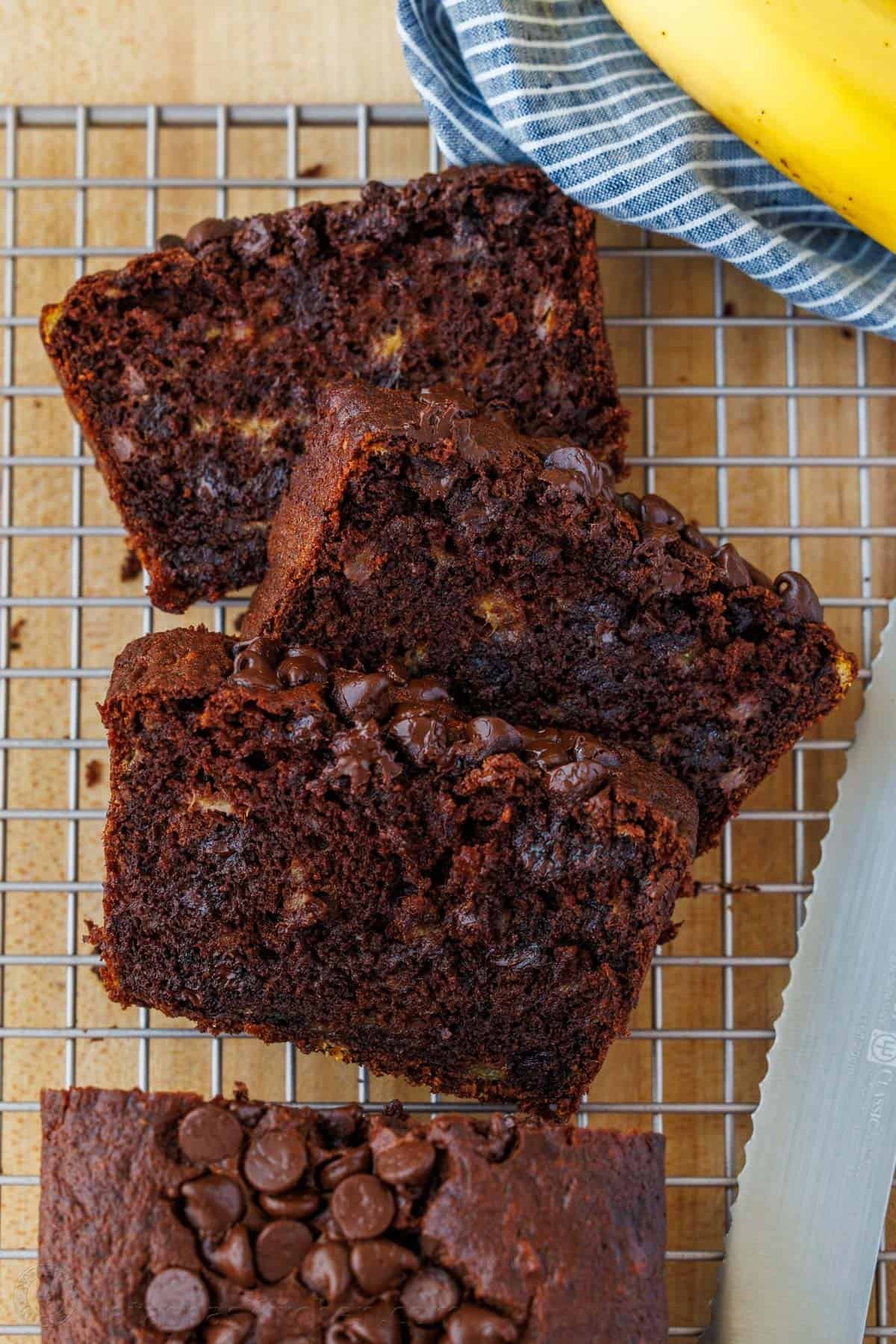 Our Chocolate Banana Bread is easy to make, extra chocolatey (with cocoa and chocolate chips), and stays moist for days. Three slices of chocolate chocolate chip banana bread on a wire cooling rack