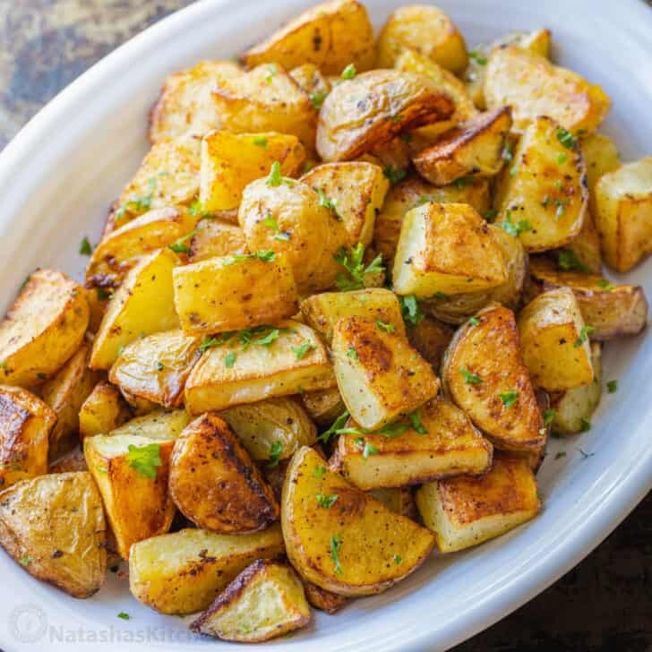 Perfect roasted potatoes in a white serving dish, garnished with parsley.