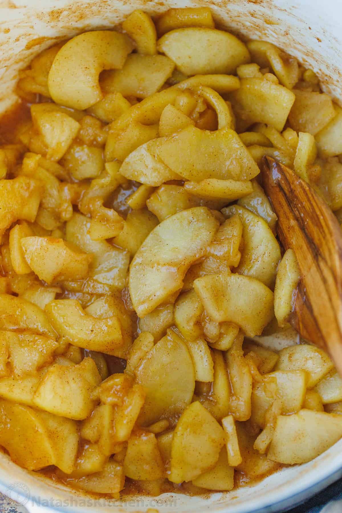 Easy sauteed cinnamon apples taste just like the filling in a cozy apple pie. Quick to make and perfect as a topping for breakfast or dessert. Sauteed cinnamon apples in a large pot with a wooden spoon.