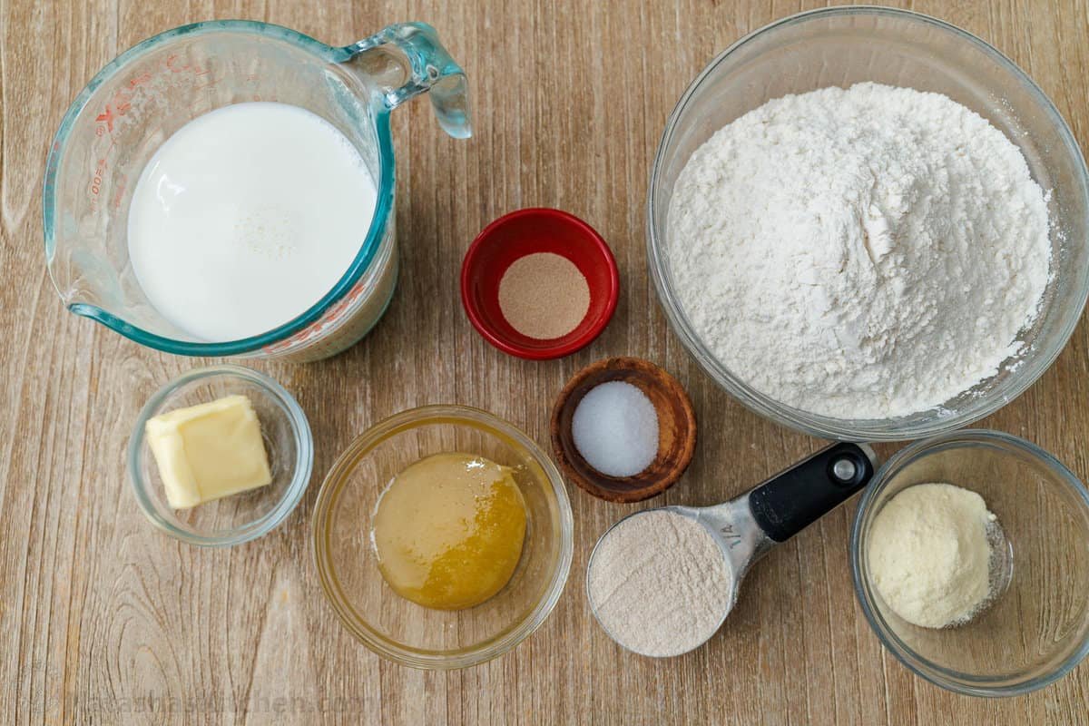 ingredients for making breakfast bread including milk, butter, honey, yeast, salt, cornmeal, bread flour and whole wheat flour