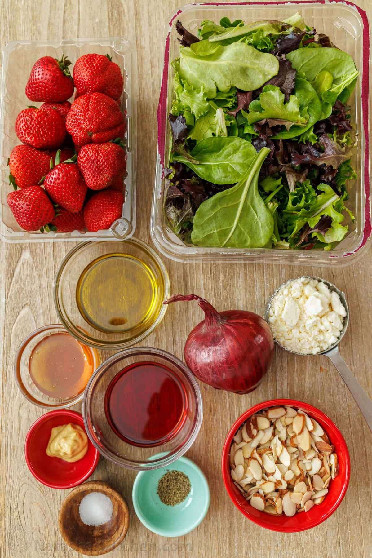 Our summer Strawberry Salad with Honey Vinaigrette is both beautiful and delicious with toasted almonds and feta. Serve in just 10 minutes! ingredients for summer side dish including spring mix greens, strawberries, olive oil, red wine vinegar, honey, salt, pepper, red onion, feta cheese and toasted almonds