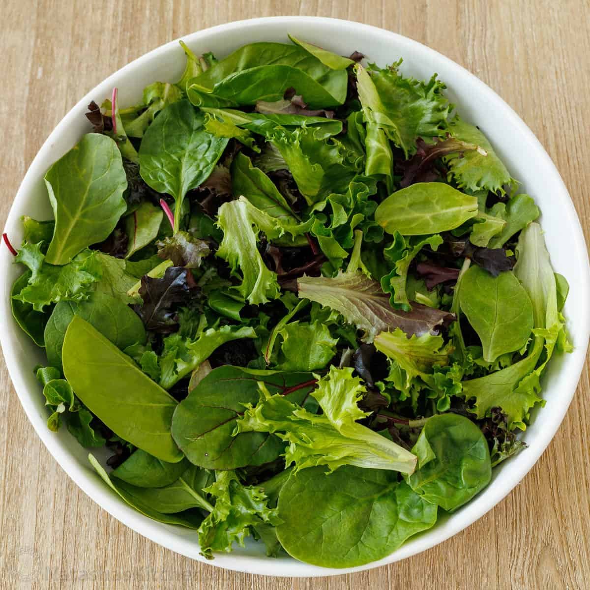 Our summer Strawberry Salad with Honey Vinaigrette is both beautiful and delicious with toasted almonds and feta. Serve in just 10 minutes! Spring mix greens in a white bowl
