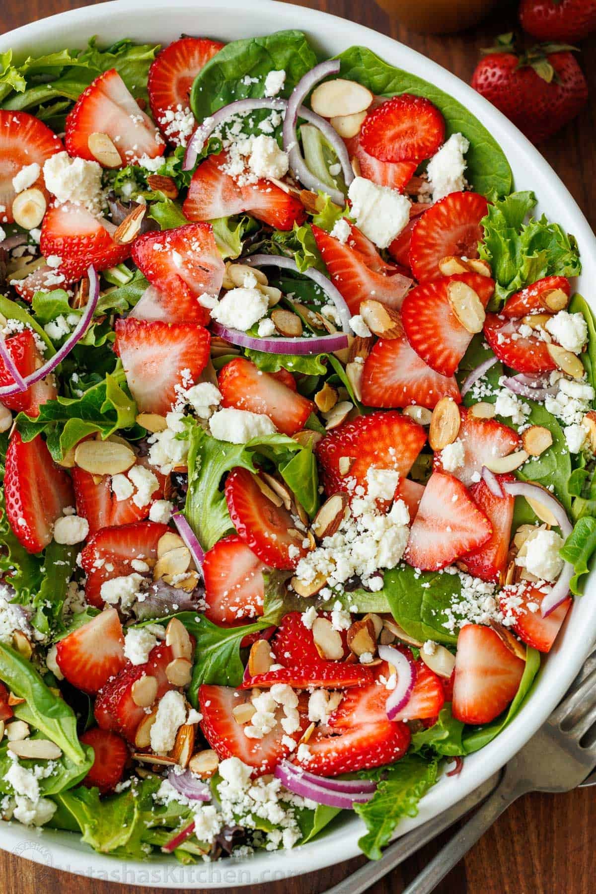 Our summer Strawberry Salad with Honey Vinaigrette is both beautiful and delicious with toasted almonds and feta. Serve in just 10 minutes! Strawberry salad recipe with feta cheese and red onions on a bed of salad greens