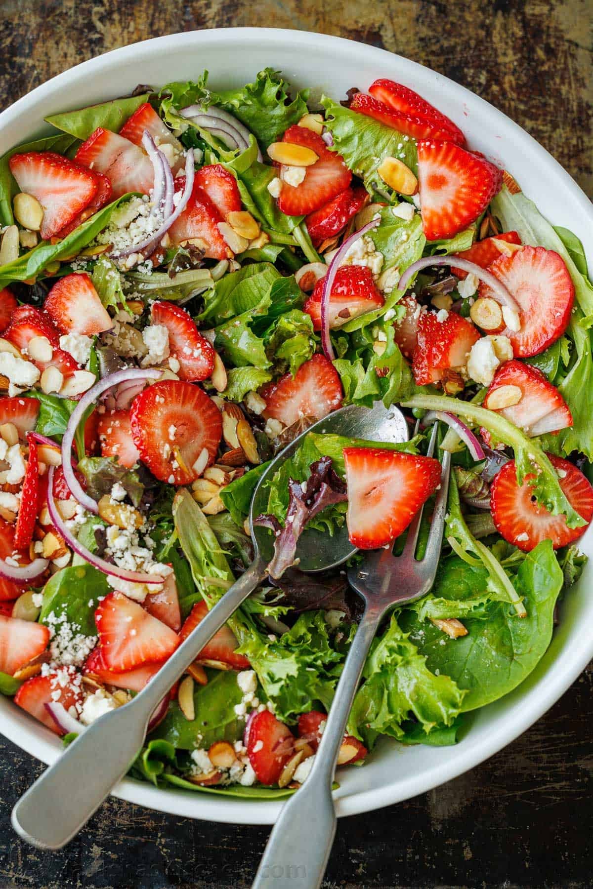 Our summer Strawberry Salad with Honey Vinaigrette is both beautiful and delicious with toasted almonds and feta. Serve in just 10 minutes! Strawberries on a bed of mixed greens and red onions