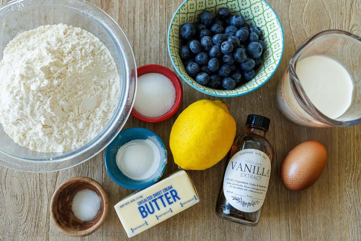 Ingredients to make blueberry scones: flour, sugar, vanilla, baking powder, lemon, butter, sugar, egg, cream