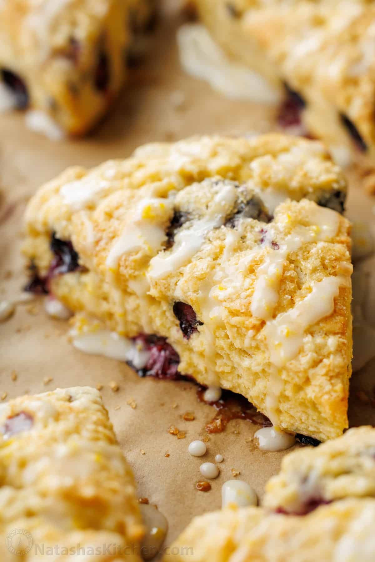 Blueberry scone wedge showing loads of berries baked in, with a lemon glaze drizzled on top