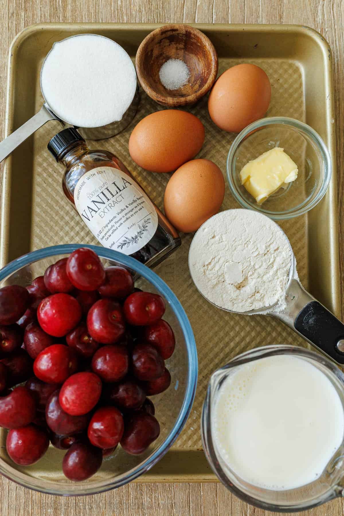 ingredients for a custard flan dessert with sugar, salt, eggs, vanilla, butter, flour, milk and cherries