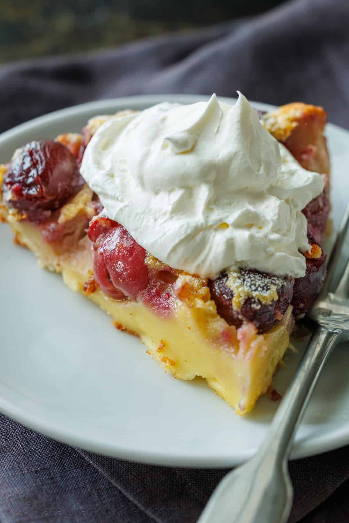 A slice of cherry custard pie on a plate with a dollop of whipped cream