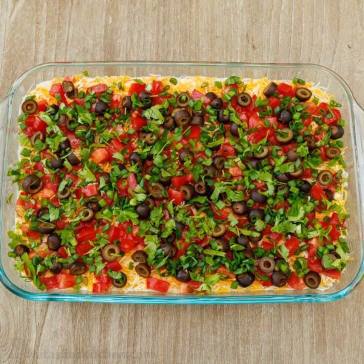 7-Layer Dip garnished with green onions and cilantro, assembled in a glass pan