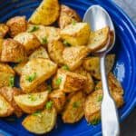 Air fryer roasted potatoes on a blue platter with a metal spoon, garnished with parsley.