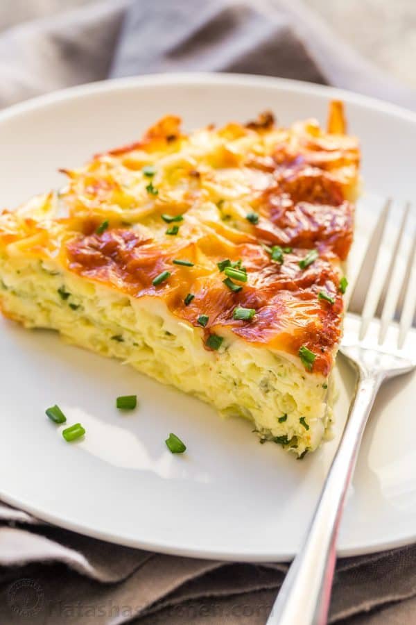 A slice of cabbage casserole on a white plate garnished with chives next to a fork