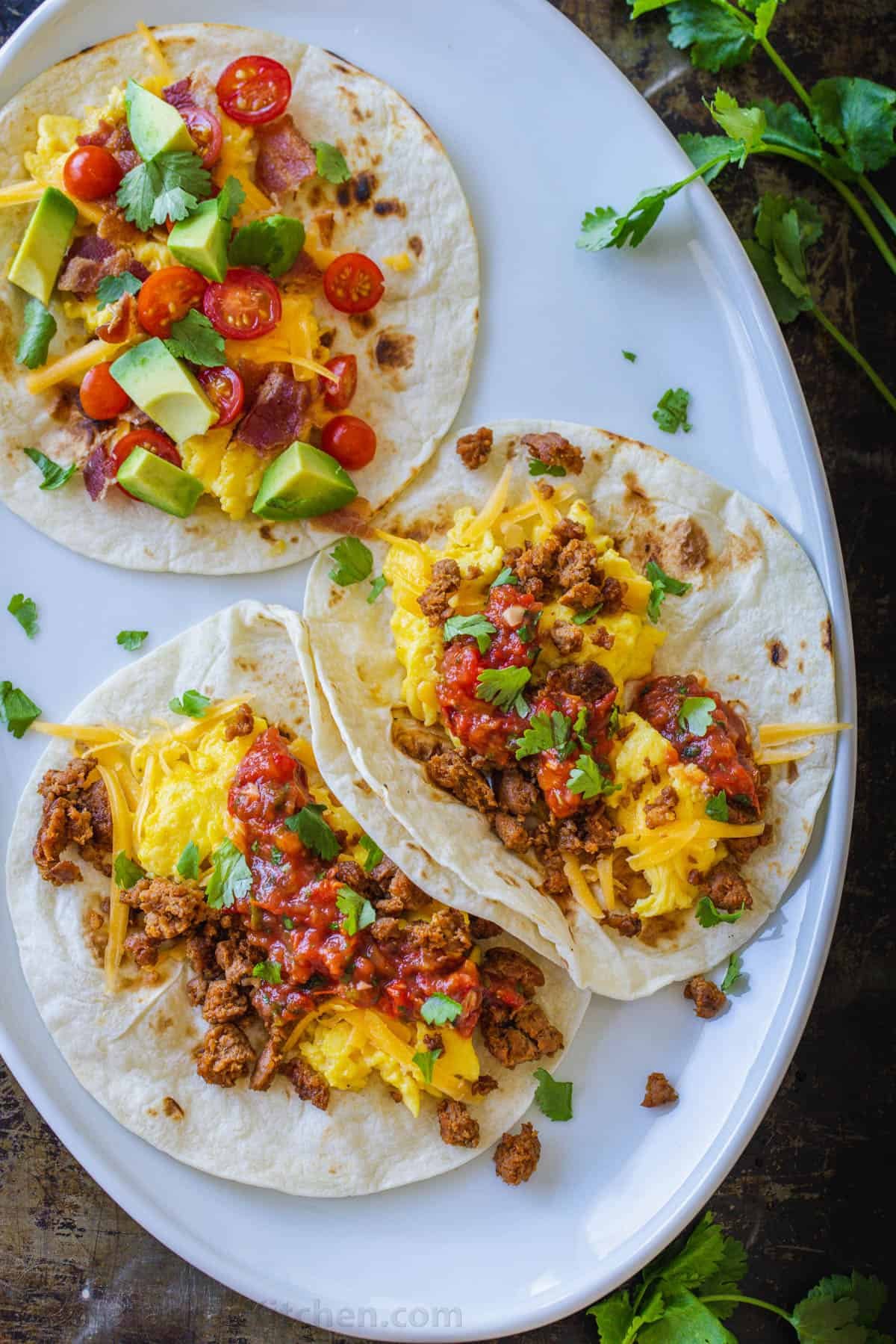 Overhead view of three breakfast tacos on a white plate.